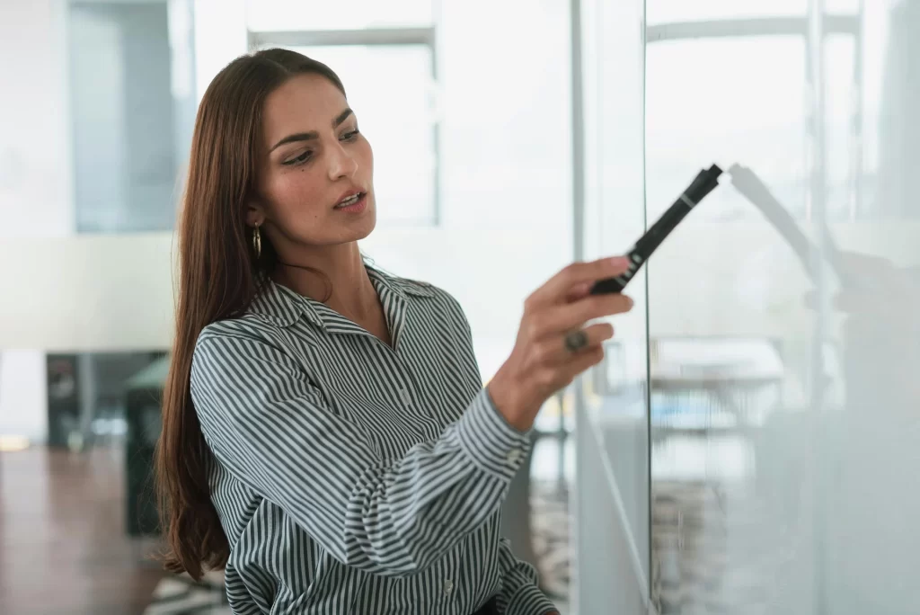 Woman delivering a training session, standing near a wall-mounted whiteboard with a marker in hand
